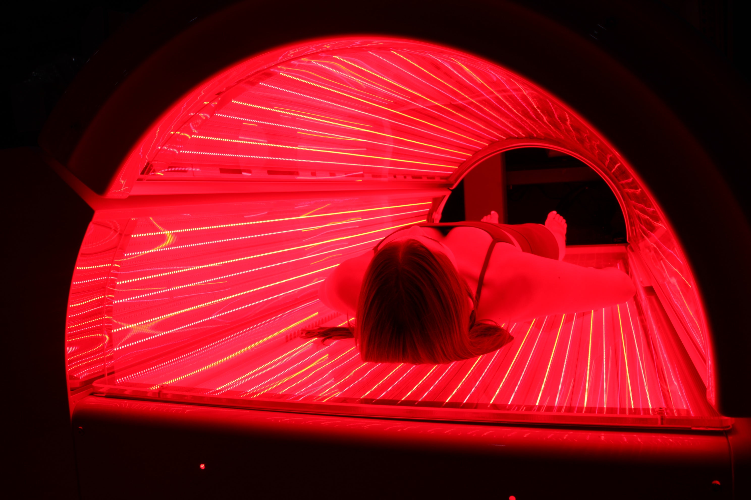 Person lying inside a red light bed by dexa plus .